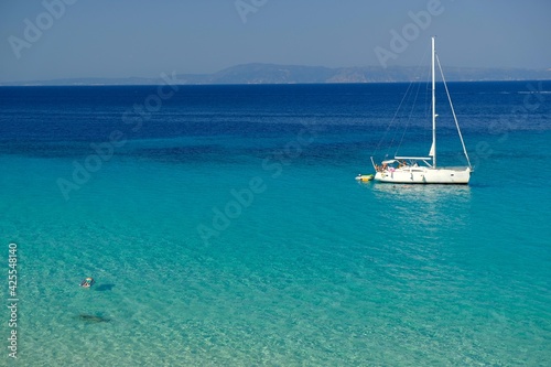Chalkidiki, Greece - August 14, 2017 : A sailboat and a single person swimming in the crystal clear waters of chalkidiki Greece