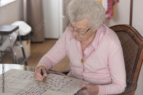 Old senior woman, 80s adult, grandmother, making crossword puzzles in her living room, a hobby for training memory.