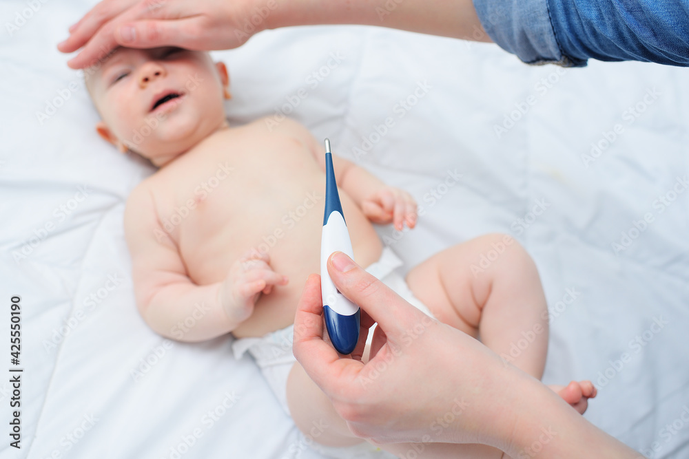 the mother holds a thermometer in one hand, and with the other hand tries the baby's forehead. the mother holds a thermometer in one hand, and with the other hand tries the baby's forehead.