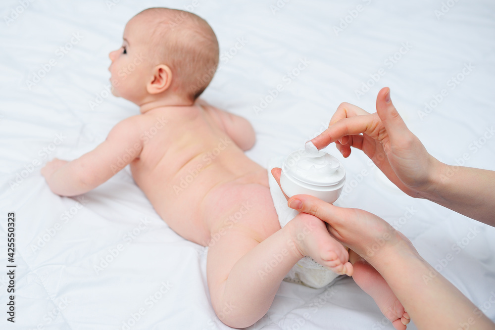 mother's hand applies a moisturizing baby cream to the baby boy's skin. Hygiene of the newborn child. mother's hand applies a moisturizing baby cream to the baby boy's skin. Hygiene of the newborn child.