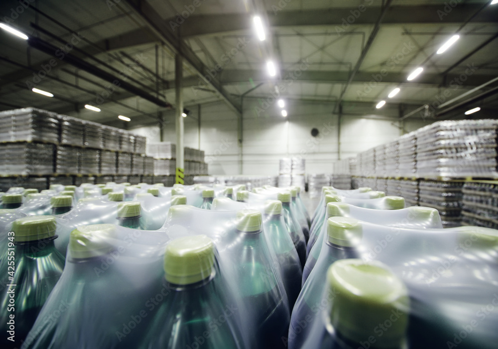 a huge industrial warehouse with plastic food wrap wrapped plastic bottles with carbonated drinks,  water or beer. - obrazy, fototapety, plakaty 