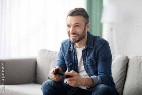 Joyful middle-aged man playing video games at home
