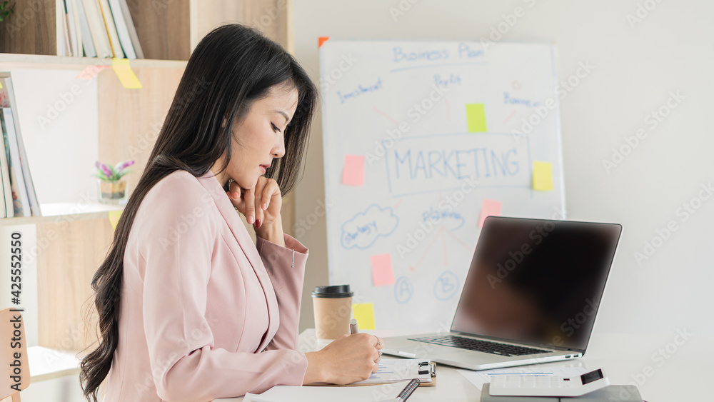 A beautiful Asian businesswoman works with documents, graphs, analyzes, and uses a laptop to work from home to create a social distance. A beautiful Asian businesswoman works with documents, graphs, analyzes, and uses a laptop to work from home to create a social distance.