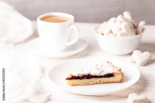 Vegan pie stuffed with cherries. Prepared without milk or eggs. In the background, a coffee with almond milk and vegan heart-shaped cookies. Photograph of breakfast in white colors