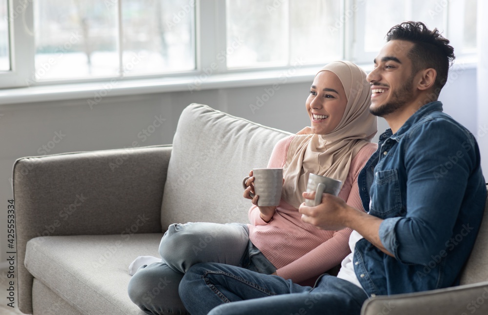 Joyful arab couple drinking coffee and looking at copy space