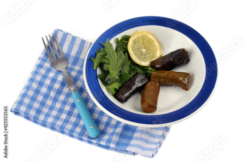 Feuilles de vigne farcies servies dans une assiette avec une rondelle de citron et de la salade roquette en gros plan sur fond blanc photo