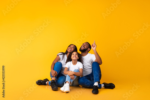 Fotografija Smiling black family pointing up at free copy space