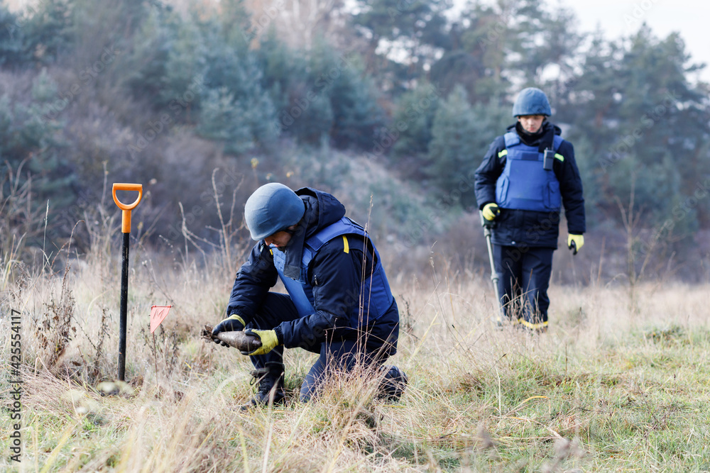 A man in a special suit works with a detector and found an explosive device. Dangerous work