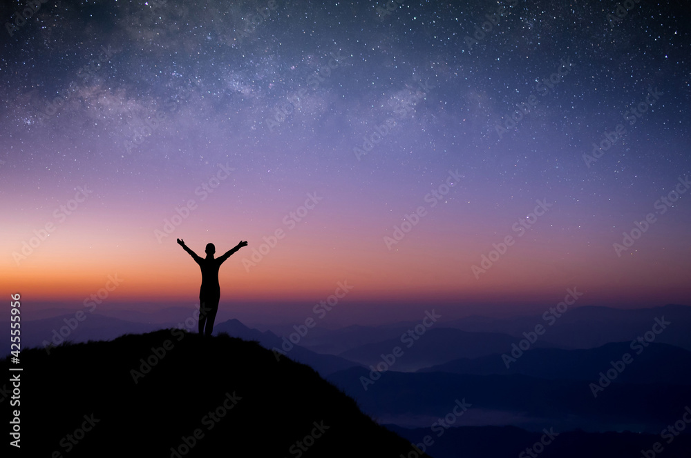 Silhouette of young female traveler standing and open arms  watched the star and milky way alone on top of the mountain with sun light in the morning.