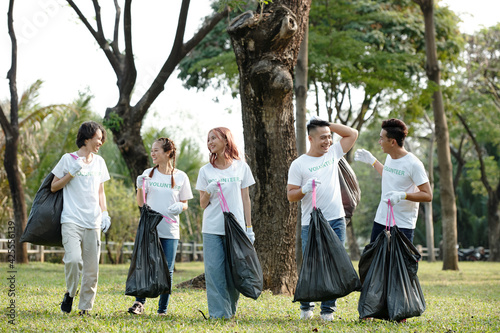 Joyful young volunteers holding plastic bags when cleaning park and picking up trash