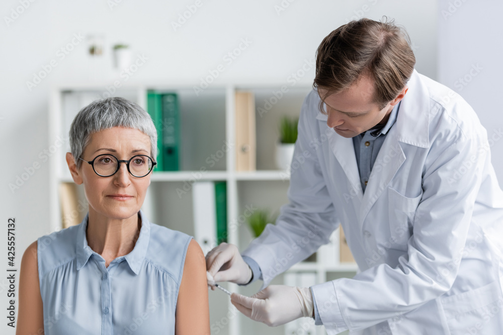 Fototapeta premium Middle aged patient sitting near doctor in latex gloves doing vaccination