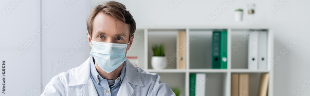 Doctor in white coat and medical mask looking at camera in hospital, banner Doctor in white coat and medical mask looking at camera in hospital, banner