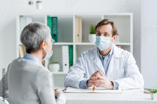 Doctor looking at patient in medical mask on blurred foreground in hospital