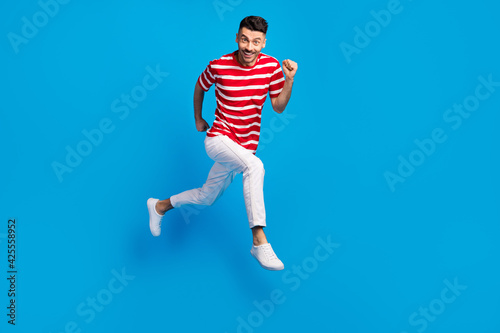 Fototapeta Naklejka Na Ścianę i Meble -  Full body profile side photo of handsome excited happy man jump up run positive weekend isolated on blue color background