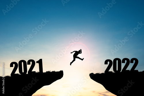 Silhouette man jumping from 2021 cliff to 2022 cliff with blue sky and sunlight, preparation new challenge business target and life for new year.