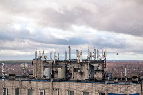 Antennas for cellular transmitters on the roof of a high-rise building. The facade of the house with windows against the background of a gloomy sky. Mobile phone tower next to housing. Radio emission © Andrei