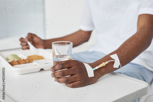 Close up of African-American man eating lunch in hospital , focus on hand with iv drip setup, copy space