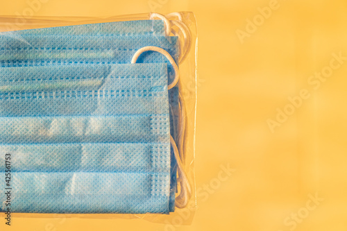 Several disposable blue medical masks in a transparent bag on a blurred disposable warm orange background. Place for your text. Close-up