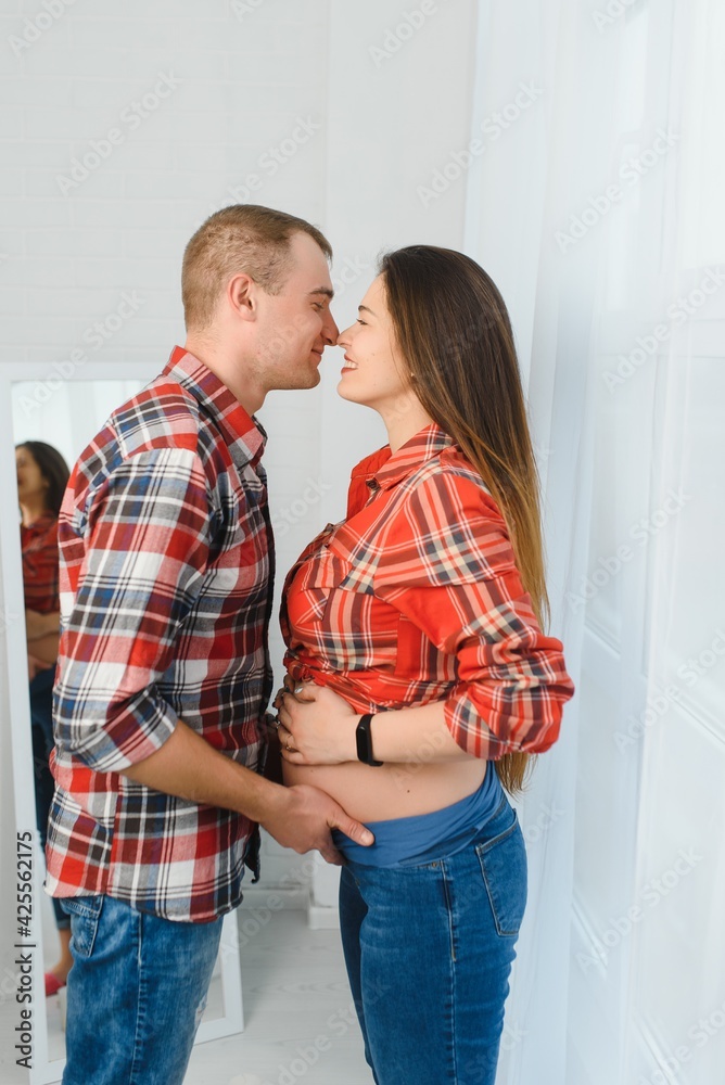 Loving man hugging his pregnant wife from behind standing near window at home, copy space Loving man hugging his pregnant wife from behind standing near window at home, copy space