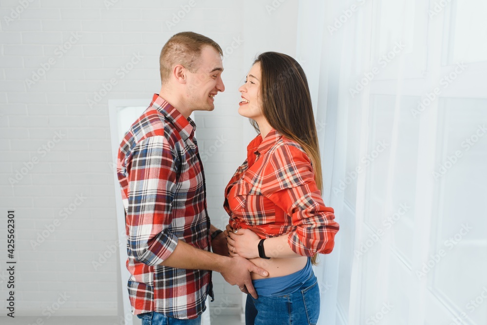 Loving man hugging his pregnant wife from behind standing near window at home, copy space Loving man hugging his pregnant wife from behind standing near window at home, copy space