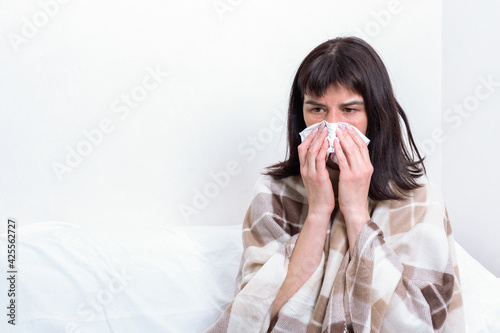 Sick day at home. Sick caucasian woman holding paper handkerchief blowing her nose, feeling unhealthy