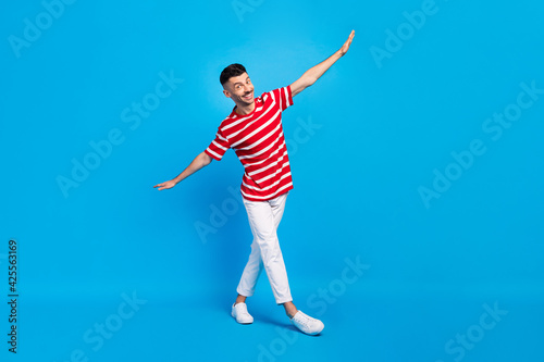 Full size photo of attractive positive young man weekend free time wings hands isolated on blue color background