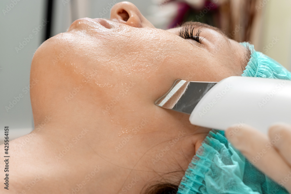 Fototapeta premium A gloved beautician cleanses the skin on the face using a special gel and equipment. The concept of facial hygiene, cosmetic procedures, skin care, skin pore cleansing, hardware cosmetology.