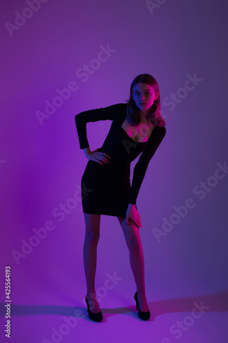 Girl portrait in neon light. Young slim woman model in black dress