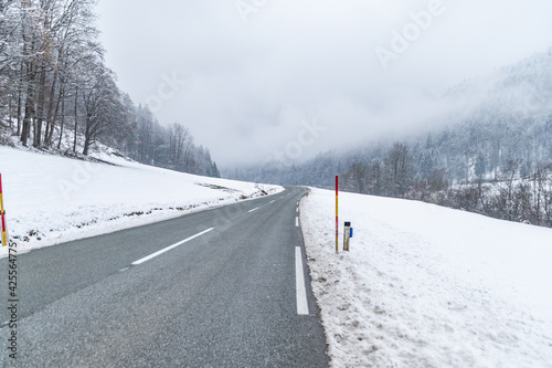 Curved countryside road in winter. Narrow Alpine valley in Slovenia. Cloudy and hazy weather. Empty path