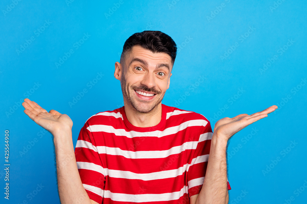 Naklejka premium Photo of funny puzzled young man wear striped t-shirt rising arms isolated blue color background