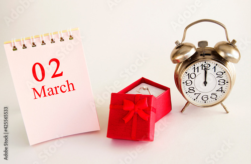 calendar date on light background with red gift box with ring and alarm clock with copy space.  March 2 is the second  day of the month photo