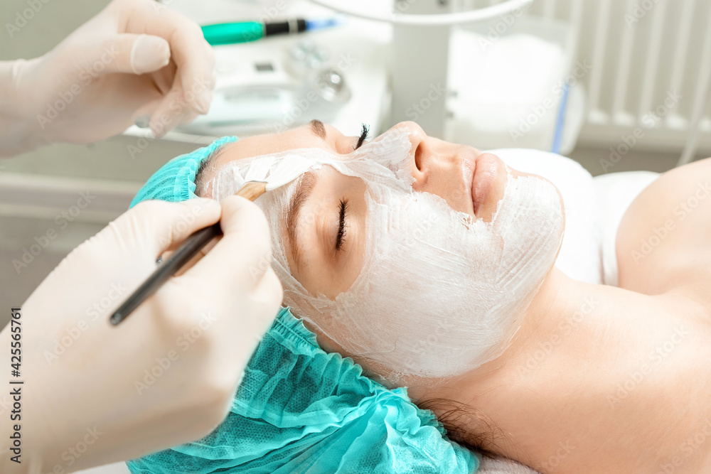 A beautician applies a mask to the face in a beauty salon. The concept of facial hygiene, cosmetic procedures, skin care, skin pore cleansing, hardware cosmetology. A beautician applies a mask to the face in a beauty salon. The concept of facial hygiene, cosmetic procedures, skin care, skin pore cleansing, hardware cosmetology.