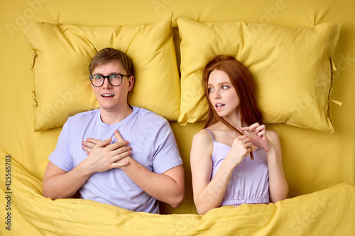 Embarrassed and shy caucasian man lying on bed with experienced excited female before his first intimacy in bed