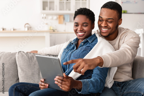 African american couple sitting on couch, using tablet