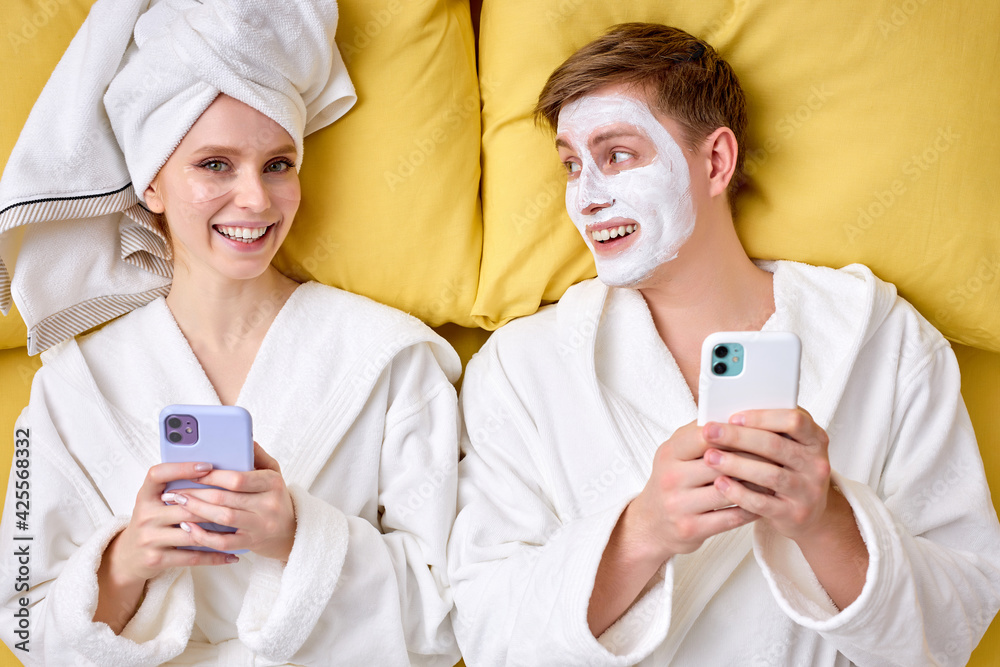 Positive married couple enjoying weekends, having rest on bed and using smartphone Positive married couple enjoying weekends, having rest on bed and using smartphone