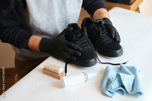 Man is cleaning sneakers in a workshop. Shoe shine service. The shoemaker prepares the shoes for the season. Shoe brush close-up. Shoe care with a special product