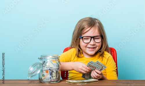 Little happy smiling kid holding charity jar with money Kid in glasses in yellow shirt counting money on table. Donate for charity