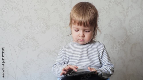 A small child holding a digital tablet and tapping the screen of an electronic device. Modern digital gadgets for early childhood development photo