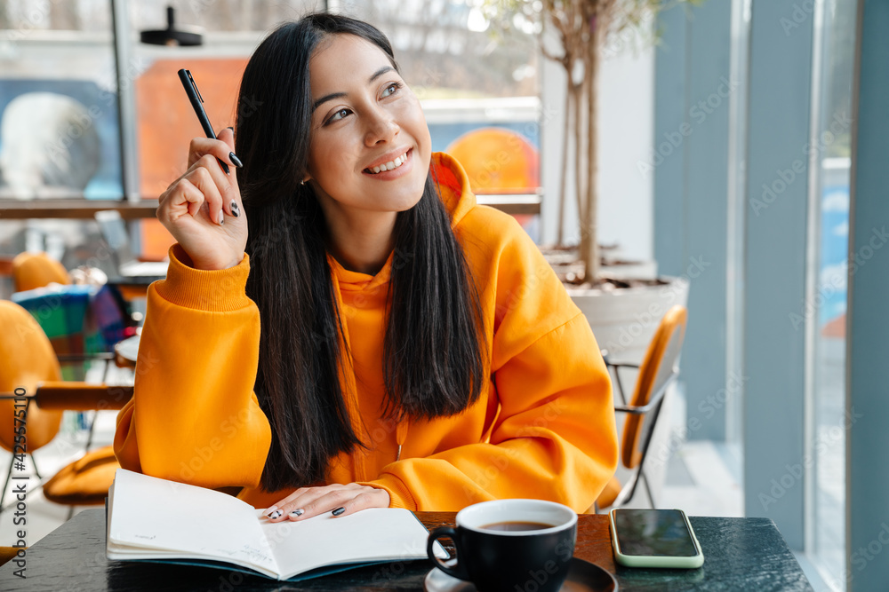 © Drobot Dean - Smiling asian woman writing down notes while sitting in cafe