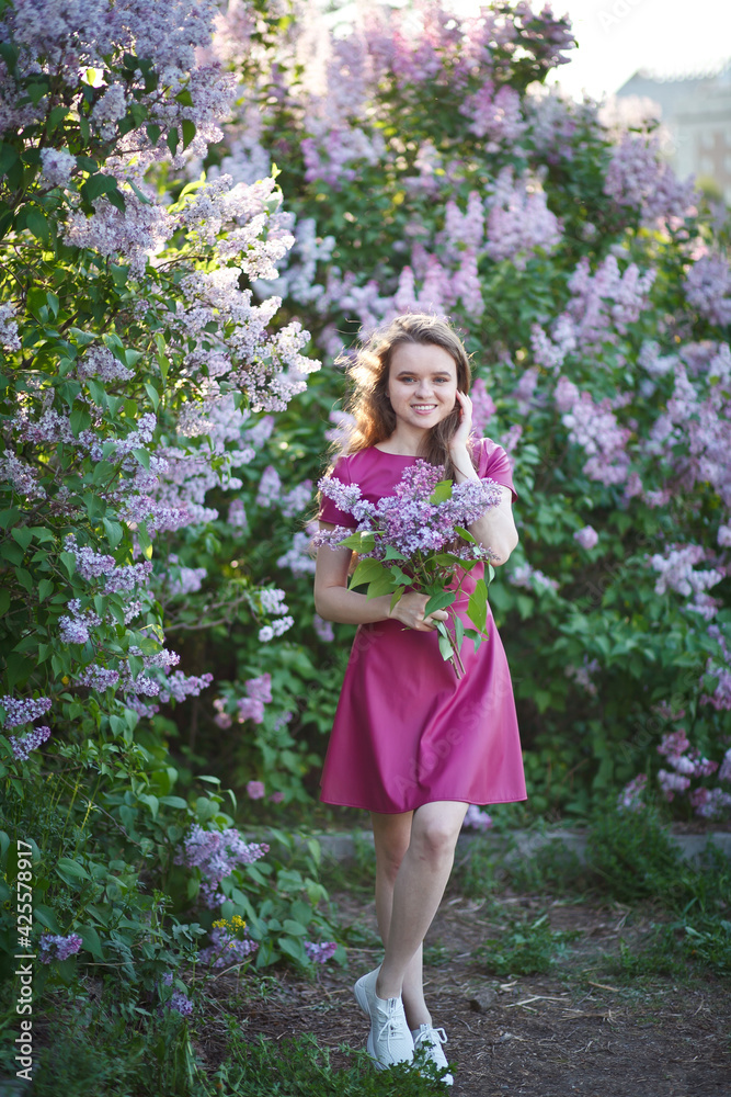 beautiful girl in a short purple dress walks in the lilac garden, leather dress, lilac bloom