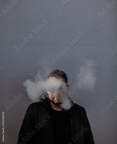 man in a leather jacket stands in a cloud of smoke