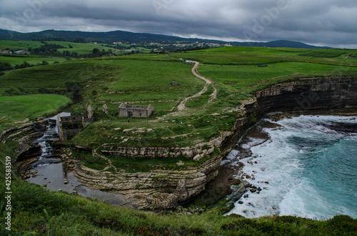 Landscape with cliffs at the sea. a river arrives and there is an old mill. Cloudy sky. boil fresh and green throughout the photo