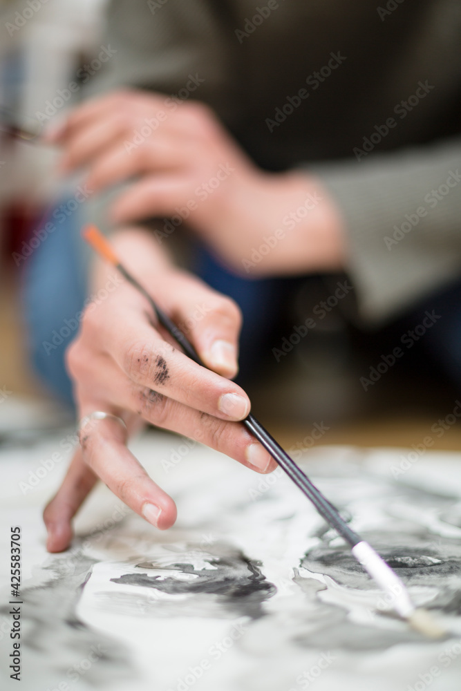 Close up of the detail of the hands of an unrecognizable artist while he is painting with watercolors on a canvas. Art concept. Selective focus. Space for text.