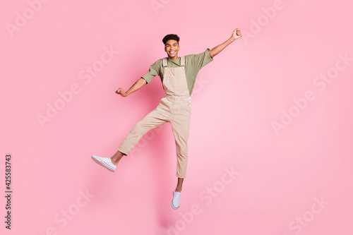 Full length body size photo of guy in overall jumping high laughing carefree dancing isolated on pastel pink color background