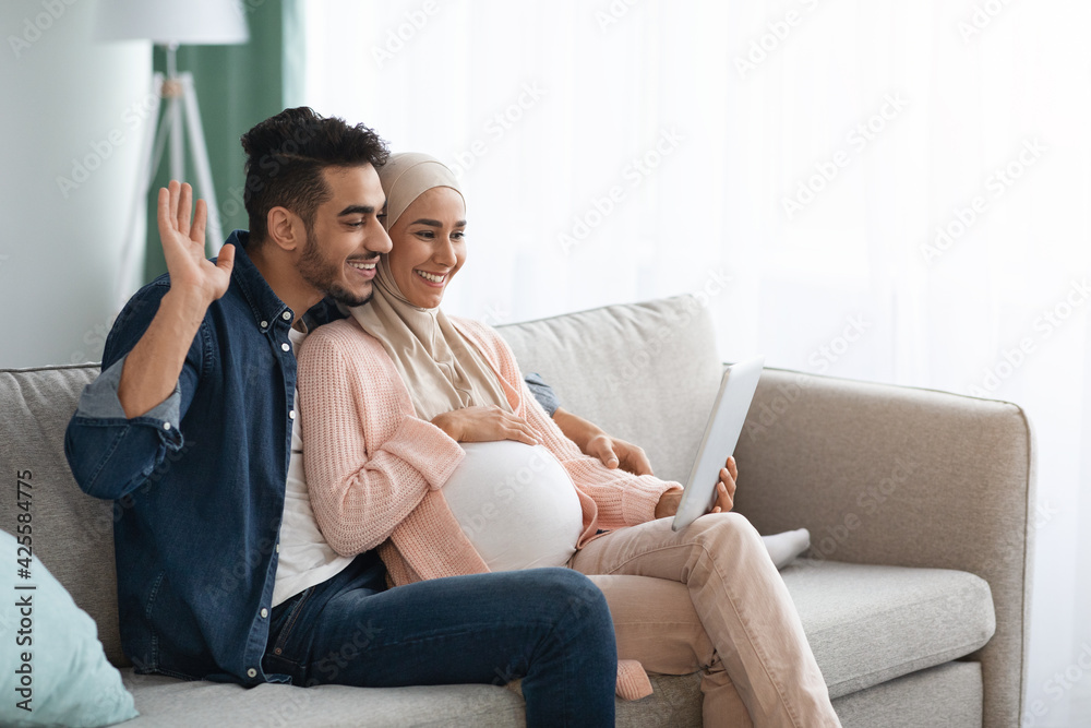 Joyful Expectant Muslim Spouses Making Video Call With Digital Tablet At Home Joyful Expectant Muslim Spouses Making Video Call With Digital Tablet At Home