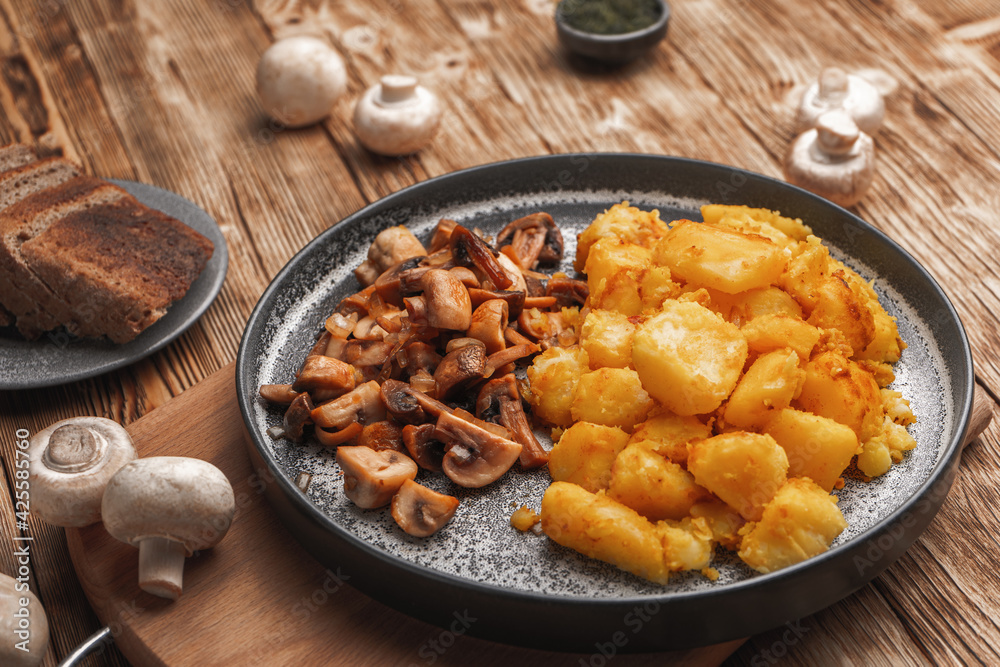Fried potatoes with mushrooms on a wooden table near fresh mushrooms