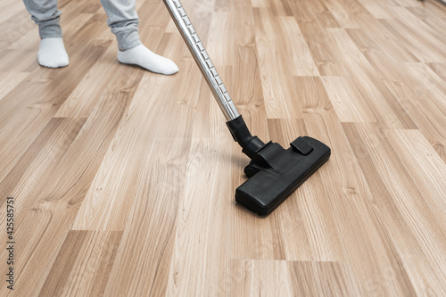 A man in white socks vacuums the wooden floor