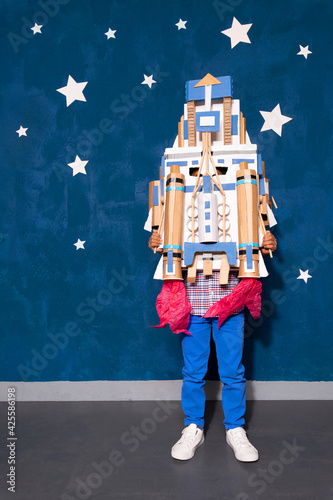 Murais de parede Rocket boy with cardboard handcrafted spacesheep posing on studio background with white paper stars