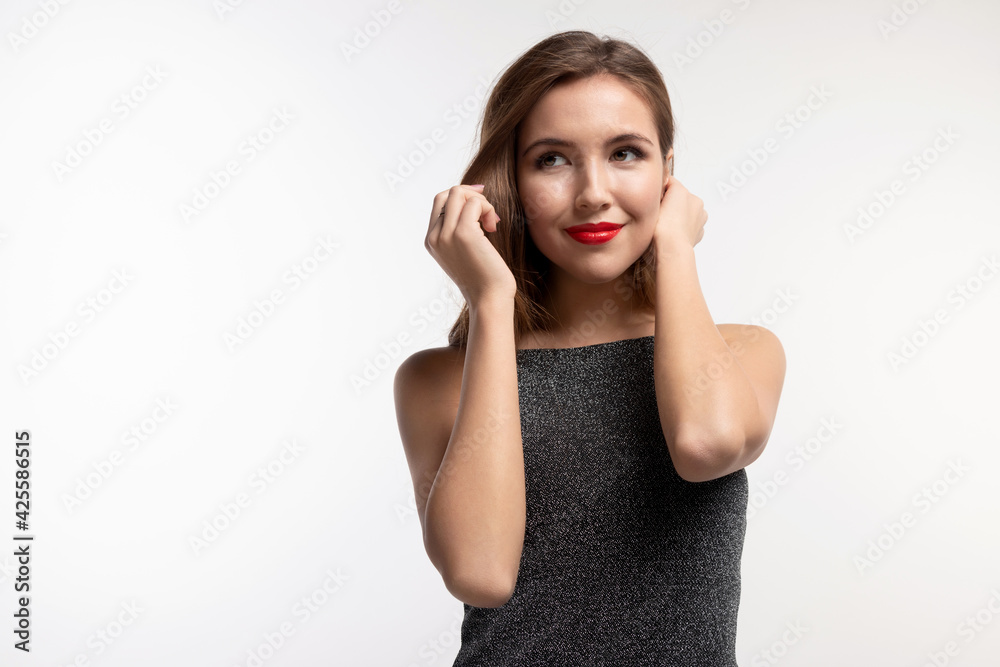 Pretty smiling young female model with bright make up, red lips posing for studio photoshoot, copyspace for advertising. Modern girl wearing gray fashionable dress. Natural beauty concept. Pretty smiling young female model with bright make up, red lips posing for studio photoshoot, copyspace for advertising. Modern girl wearing gray fashionable dress. Natural beauty concept.