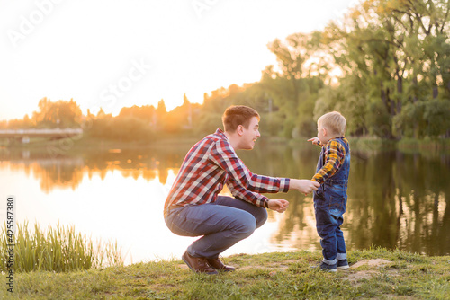 Dad and son at sunset in the summer. A happy family rests by the water on vacation. The boy points his finger at the lake.